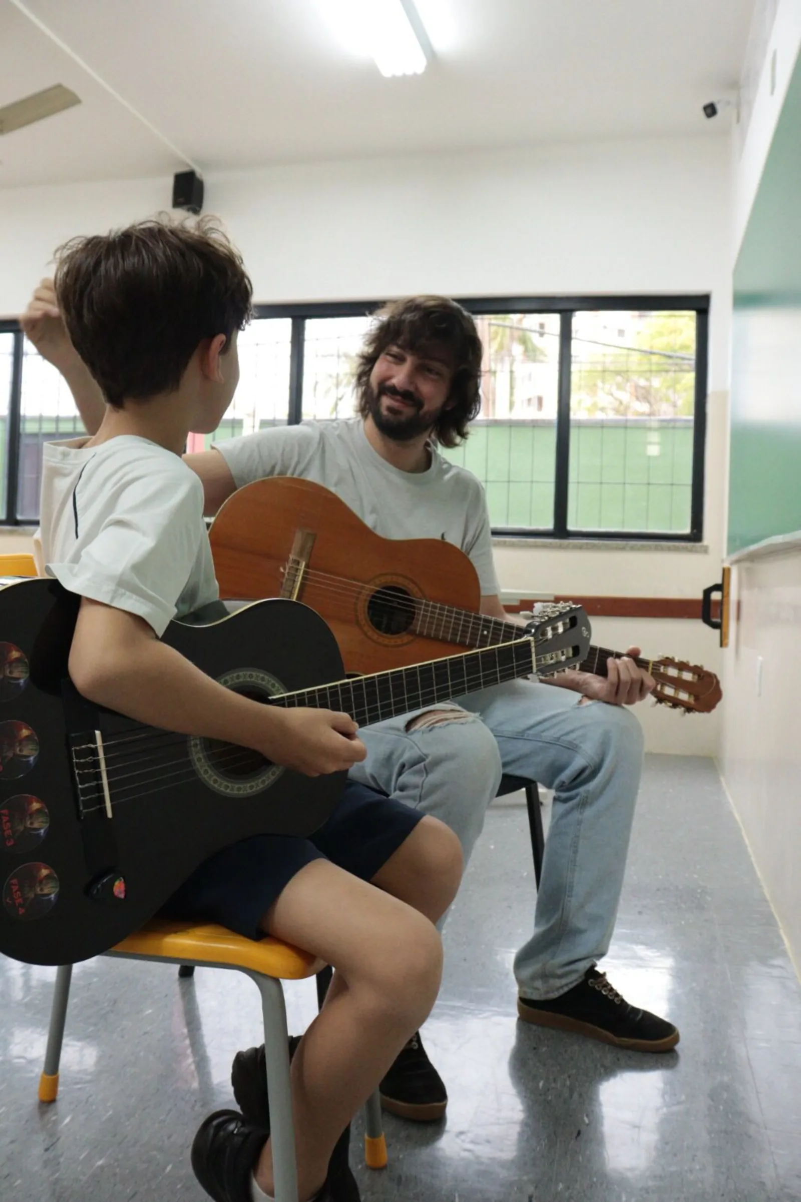 Professor e aprendiz sentados frente a frente, cada um com seu violão, durante uma aula